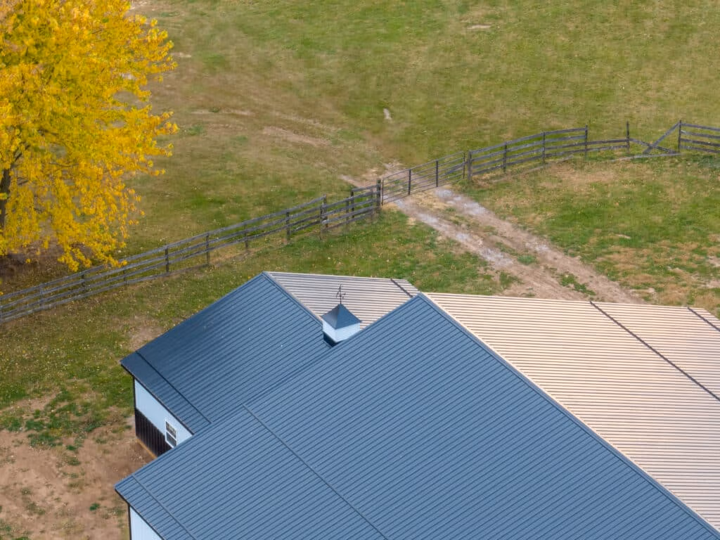 Aerial view of a building with dark metal roof and white metal siding, surrounded by pasture and fencing