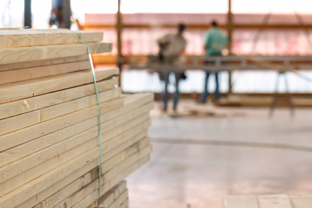 Stacked wooden lumber and plywood sheets with blurred warehouse or job site in background