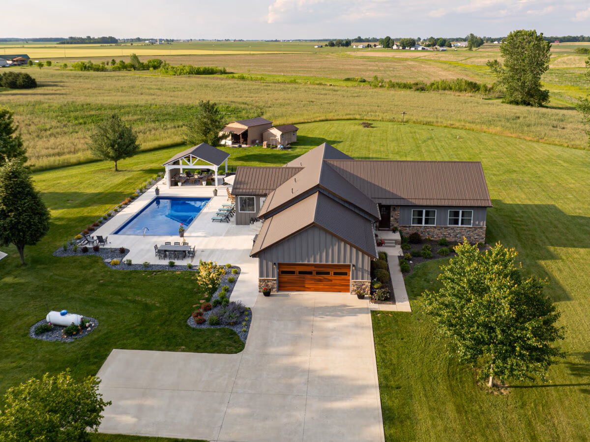 Residential home with dark metal roof and siding, featuring a pool and circular driveway on manicured lawn in rural Ohio setting