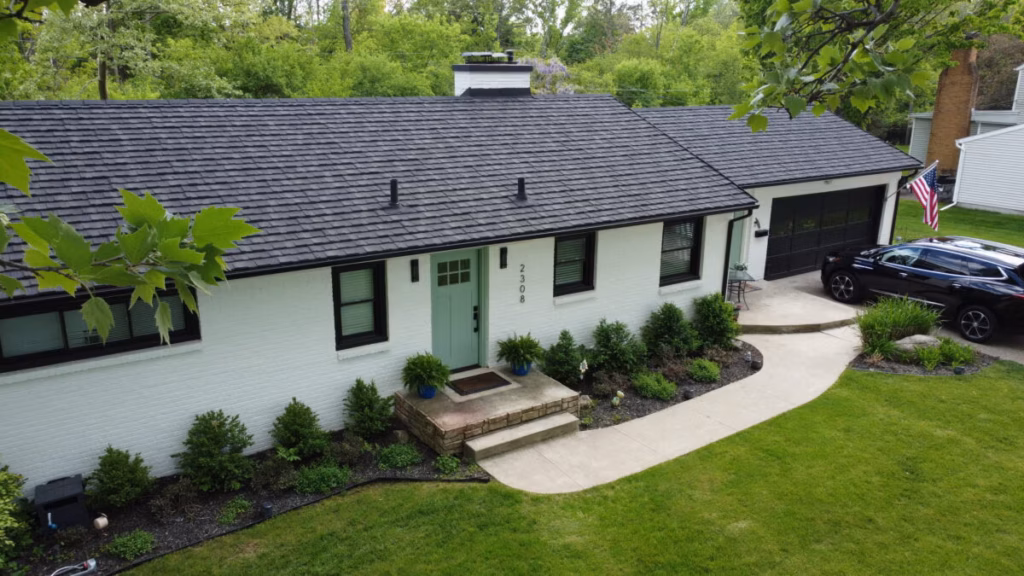 Single-story home with charcoal metal shingle roof, white siding, black windows, and manicured lawn with landscaping