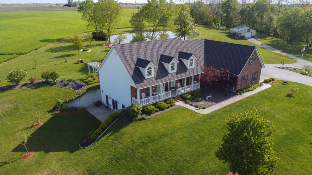 Aerial view of a two-story cottage with a metal shingle roof in Ironwood style, surrounded by green lawn and trees