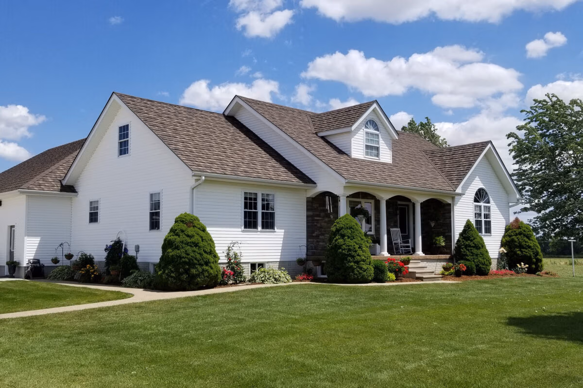 White residential home with metal shingle roof in cottage style, stone veneer accents, and manicured lawn.