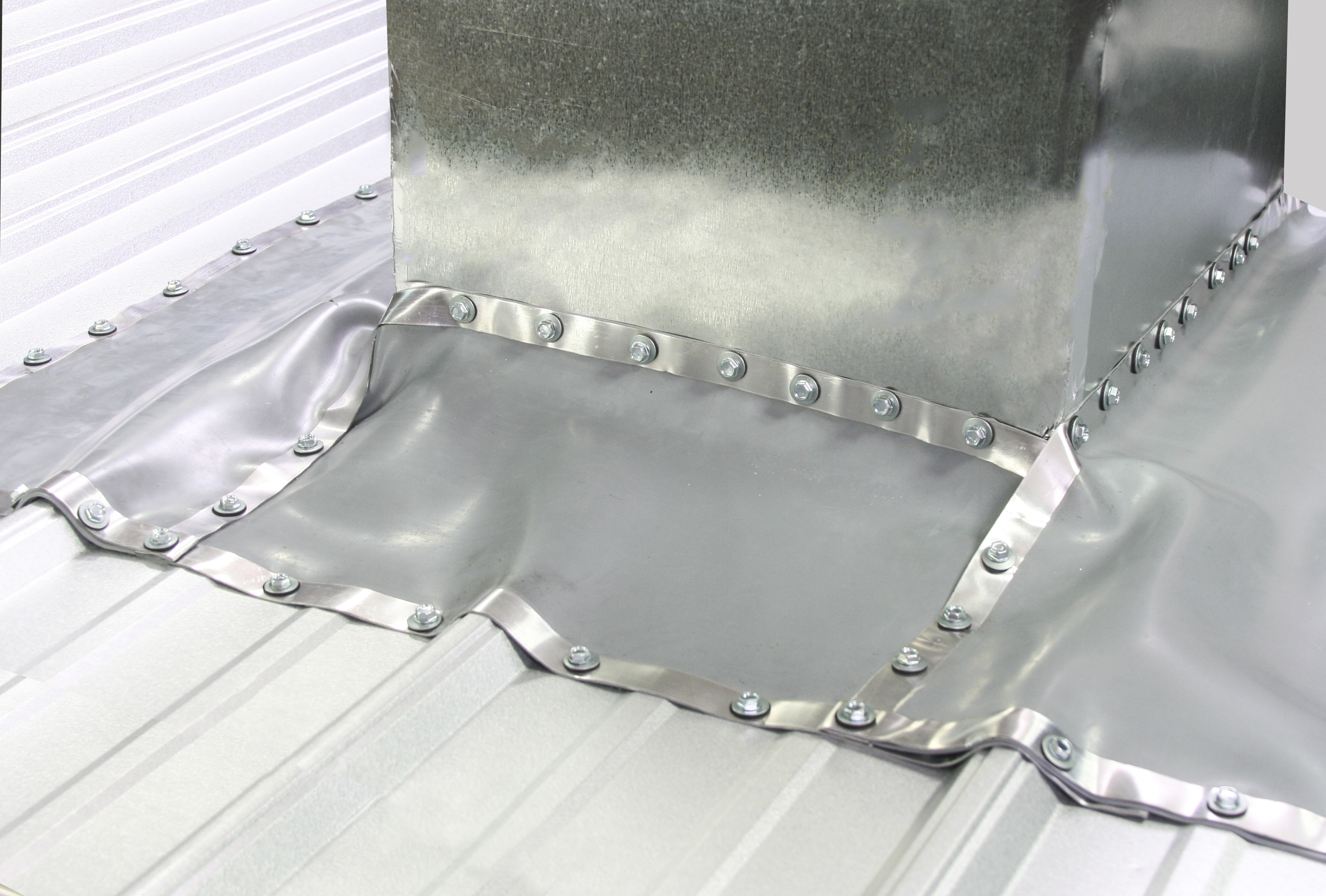 A galvanized metal roof curb base flashing with riveted expansion joint collar installed on a standing seam metal roof panel system.