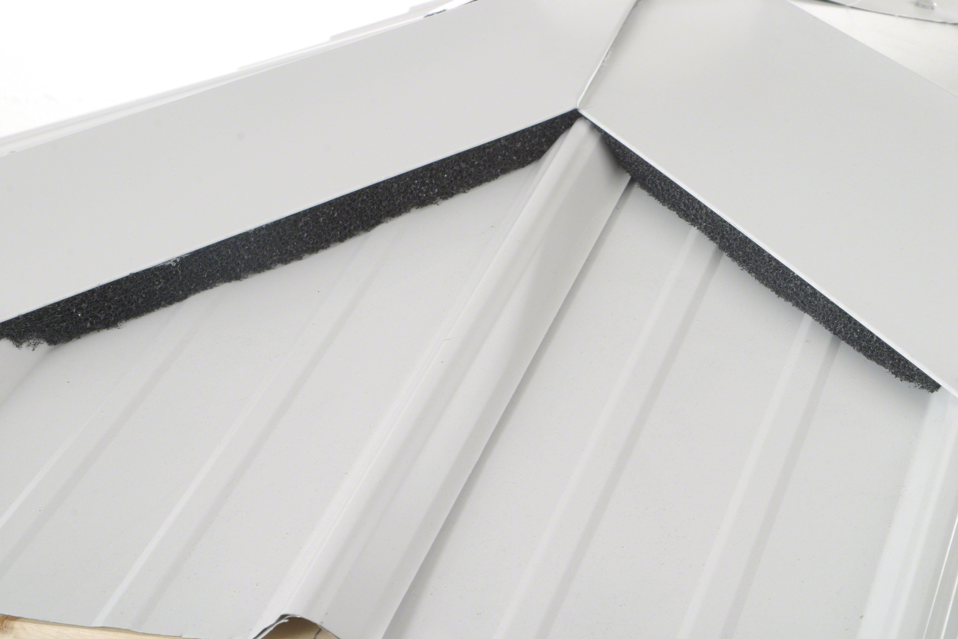 Close-up of white corrugated metal roofing panels with a black foam closure strip installed along the ridge joint to seal gaps between panels.