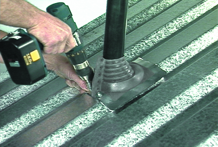 A person uses a yellow cordless drill to fasten a rubber pipe boot flashing collar around a black pipe on a corrugated metal roof.