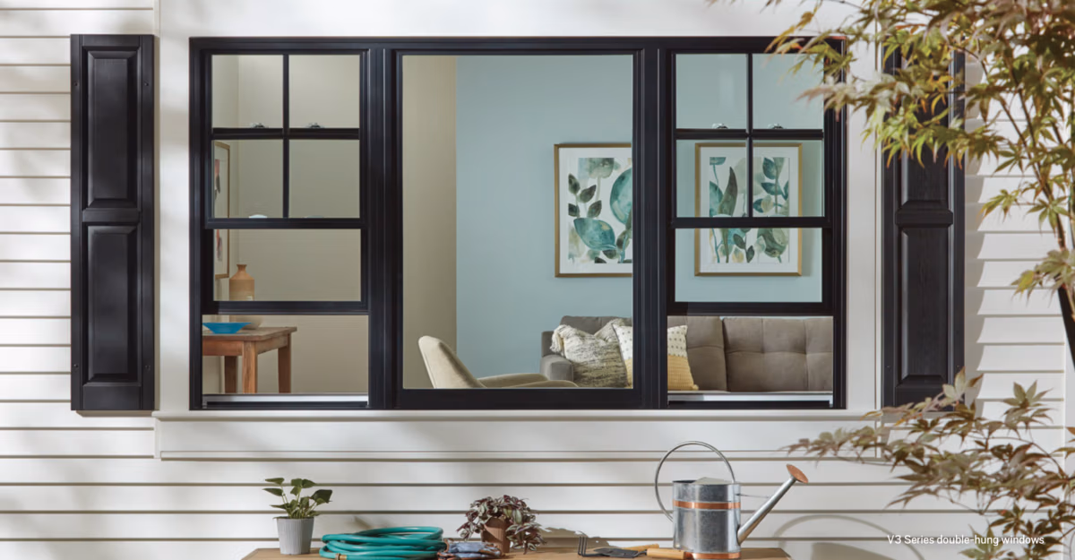 Black-framed window wall with multiple panes installed on white siding, showing interior storage shelves and blue-green wall color