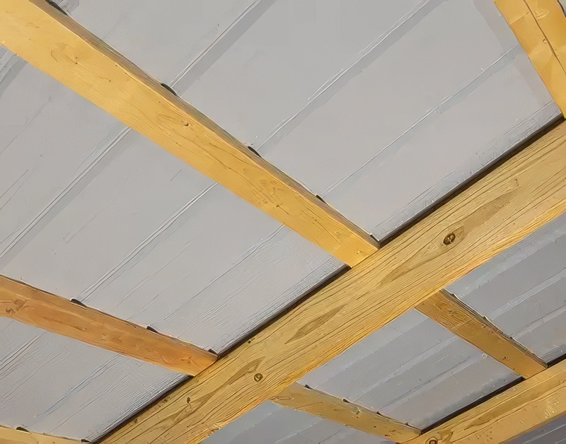 Interior view looking up at yellow pine wood framing rafters crossing over white corrugated metal roofing panels installed on a shed or outbuilding ceiling.