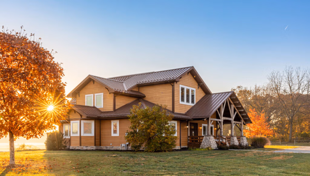 Two-story brick home with metal roof, illuminated by golden hour sunlight filtering through a large oak tree in the front yard