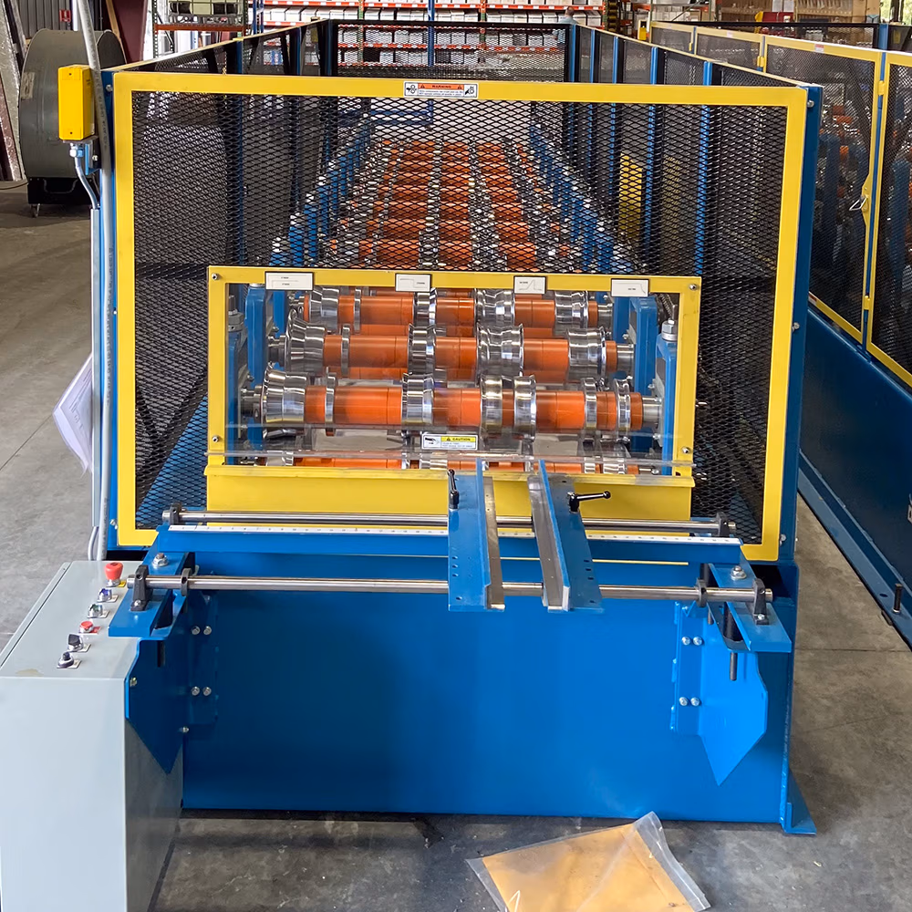 A blue and yellow roll forming machine with orange and silver rollers enclosed behind a yellow-framed black mesh safety guard, situated on a concrete factory floor.
