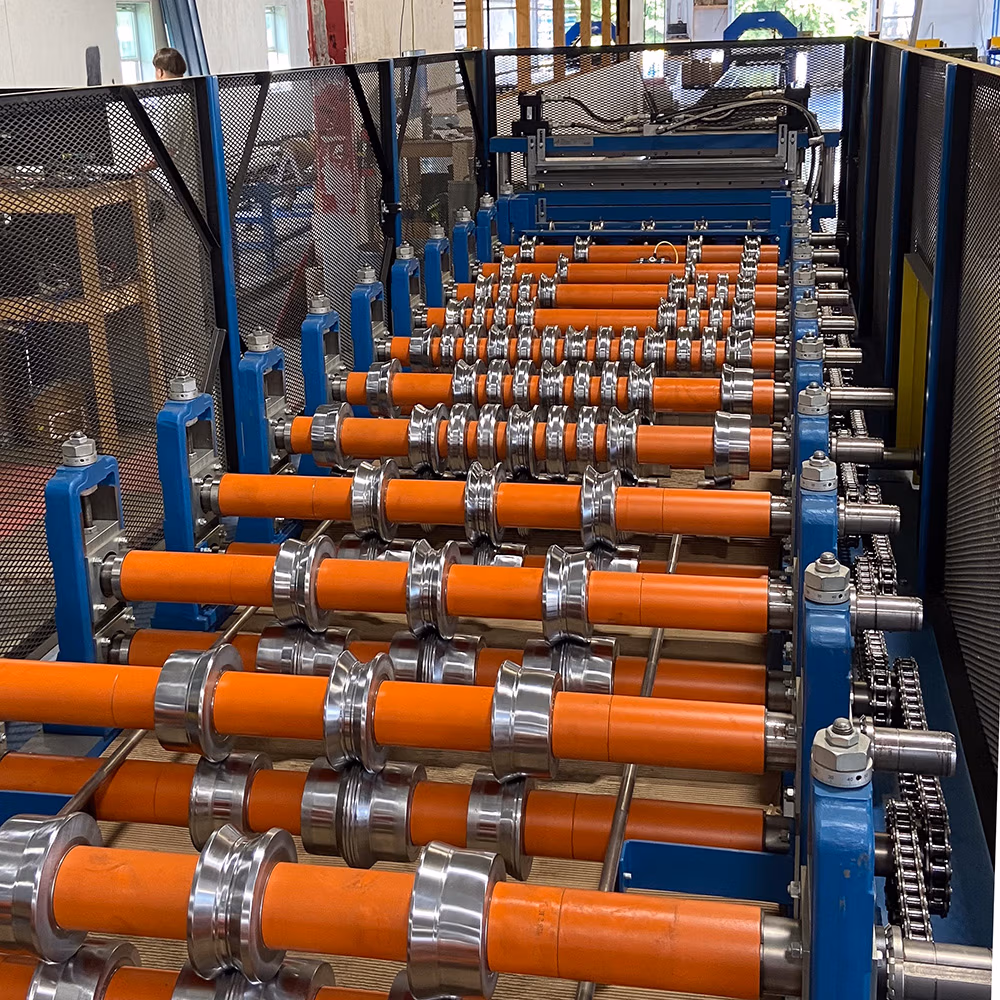 A industrial roll forming machine featuring rows of bright orange rubber rollers and silver metal forming dies mounted on a blue steel frame inside a manufacturing facility.