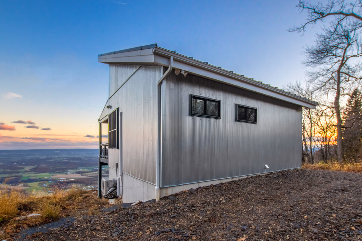 Small metal-sided structure on hillside at sunset, demonstrating corrugated panel installation on exterior walls