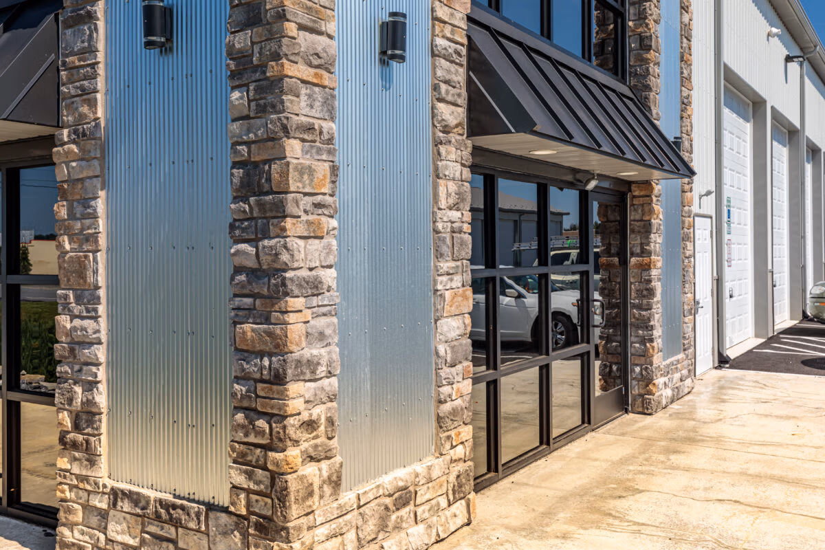 Building exterior with vertical corrugated metal panels in light blue-gray, paired with brick and modern black-framed windows and door.