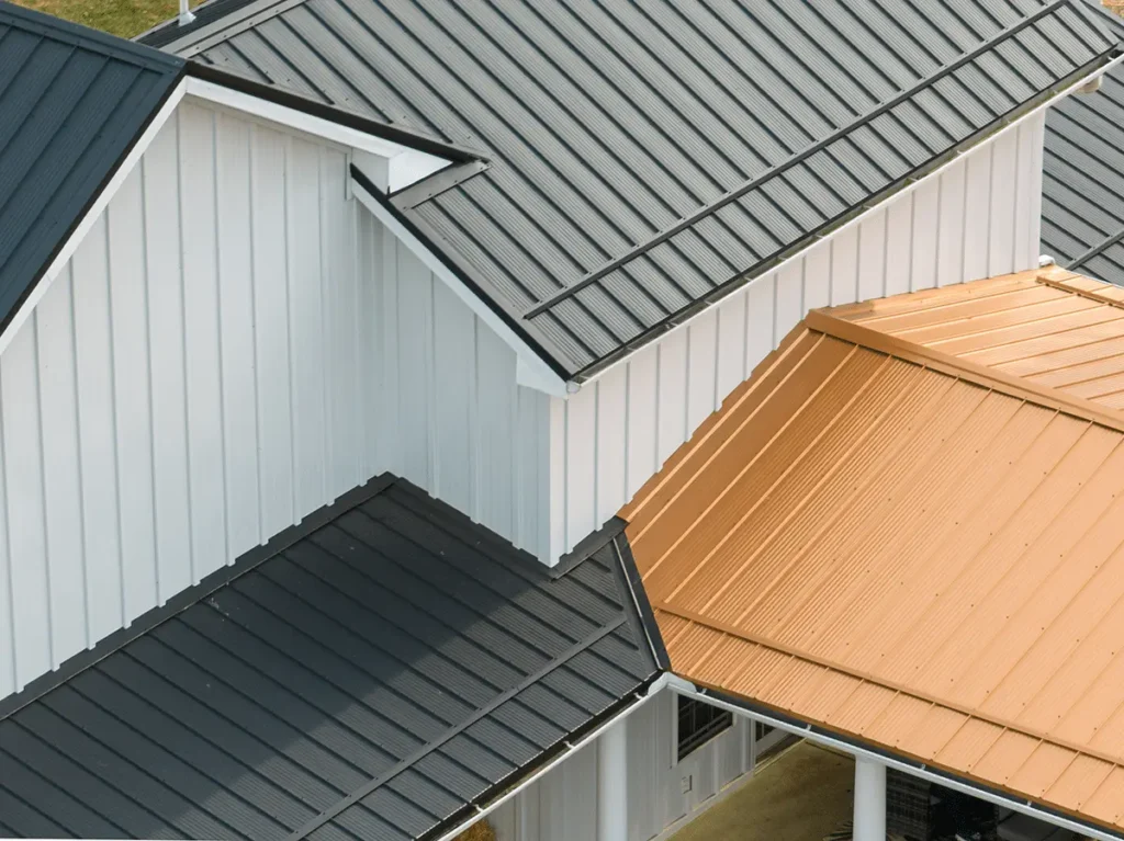 Aerial view of intersecting residential rooflines featuring dark charcoal gray and warm copper-toned standing seam metal panels contrasted against white vertical board-and-batten siding.