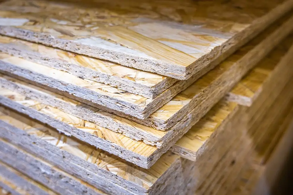 Multiple sheets of oriented strand board (OSB) stacked in a neat pile, showing the characteristic wood strand texture on the surface and layered compressed wood fiber edges.