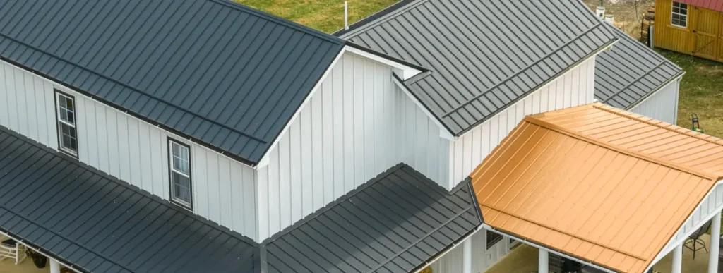 Aerial view of a white board-and-batten building featuring Buckeye wave standing seam metal roof panels in charcoal black on the main structure and warm copper penny accent panels on the porch and attached addition.