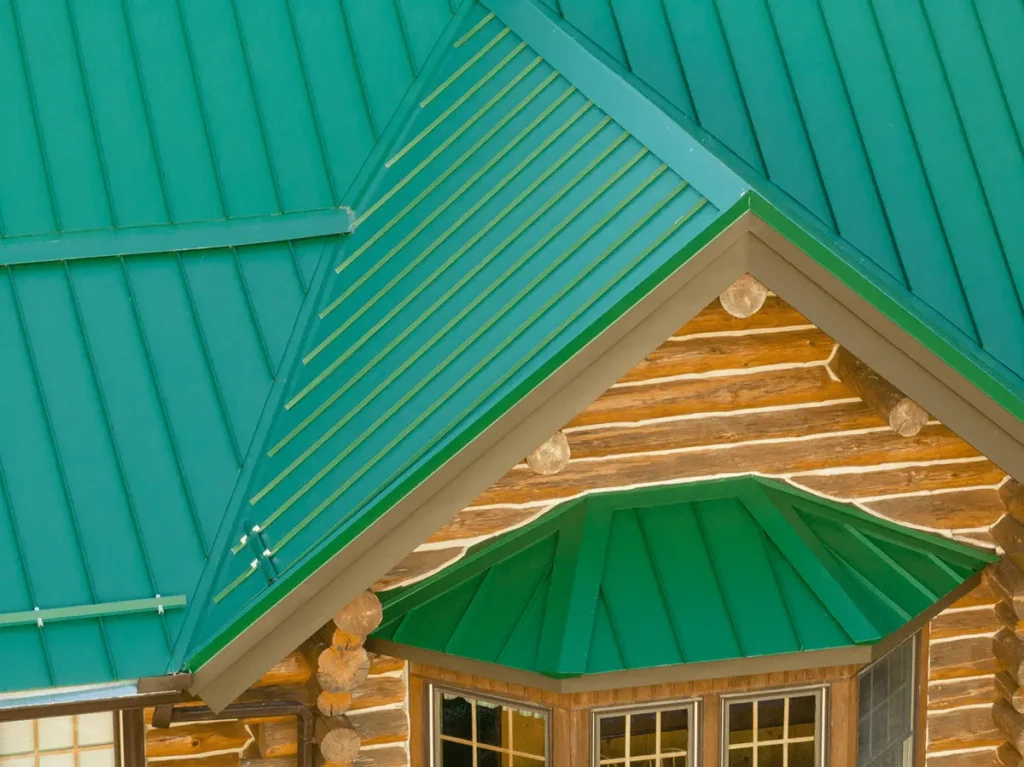 An aerial close-up view of a log cabin featuring a vibrant teal standing seam metal roof with a gabled dormer entry, exposed log ends, and multi-pane windows.