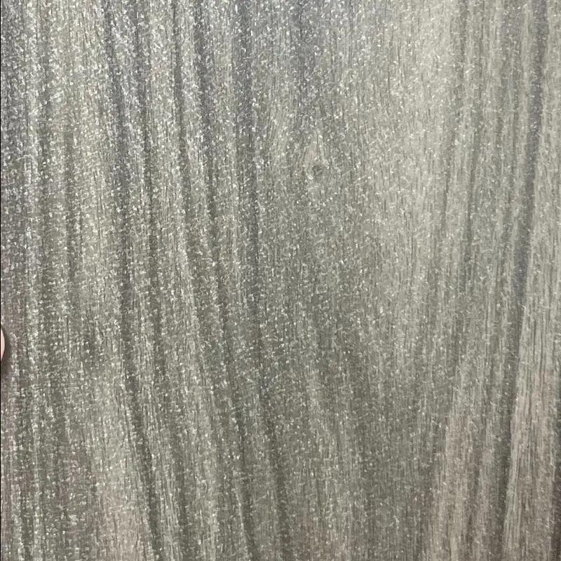 A close-up view of a gray wood-grain decorative panel showing vertical streaks, natural knot patterns, and silvery highlights that mimic real wood grain.