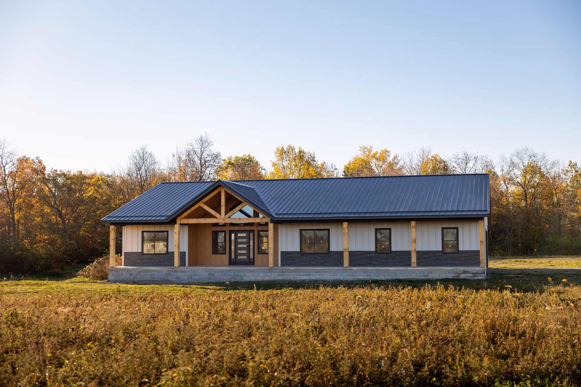 Single-story residential home with tan metal siding and 5-V Crimp metal roof in rural setting surrounded by open field