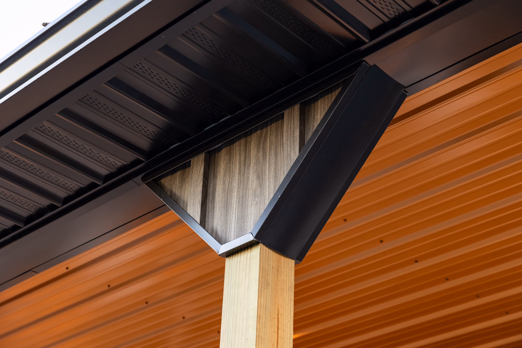 Close-up of a black metal gutter with white soffit and brown corrugated metal siding on a residential structure