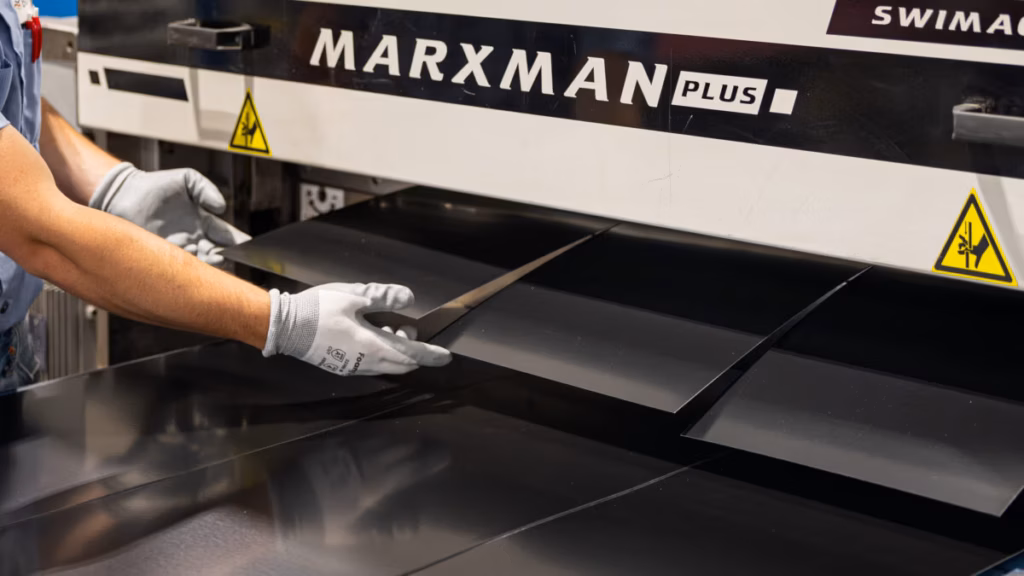 Hands installing a metal roofing panel onto a Marxman machine, showing the practical application of metal roofing products.