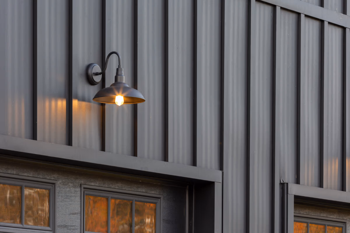 Corrugated metal siding in gray with warm-toned sconce lights mounted on the facade above windows with bronze frames