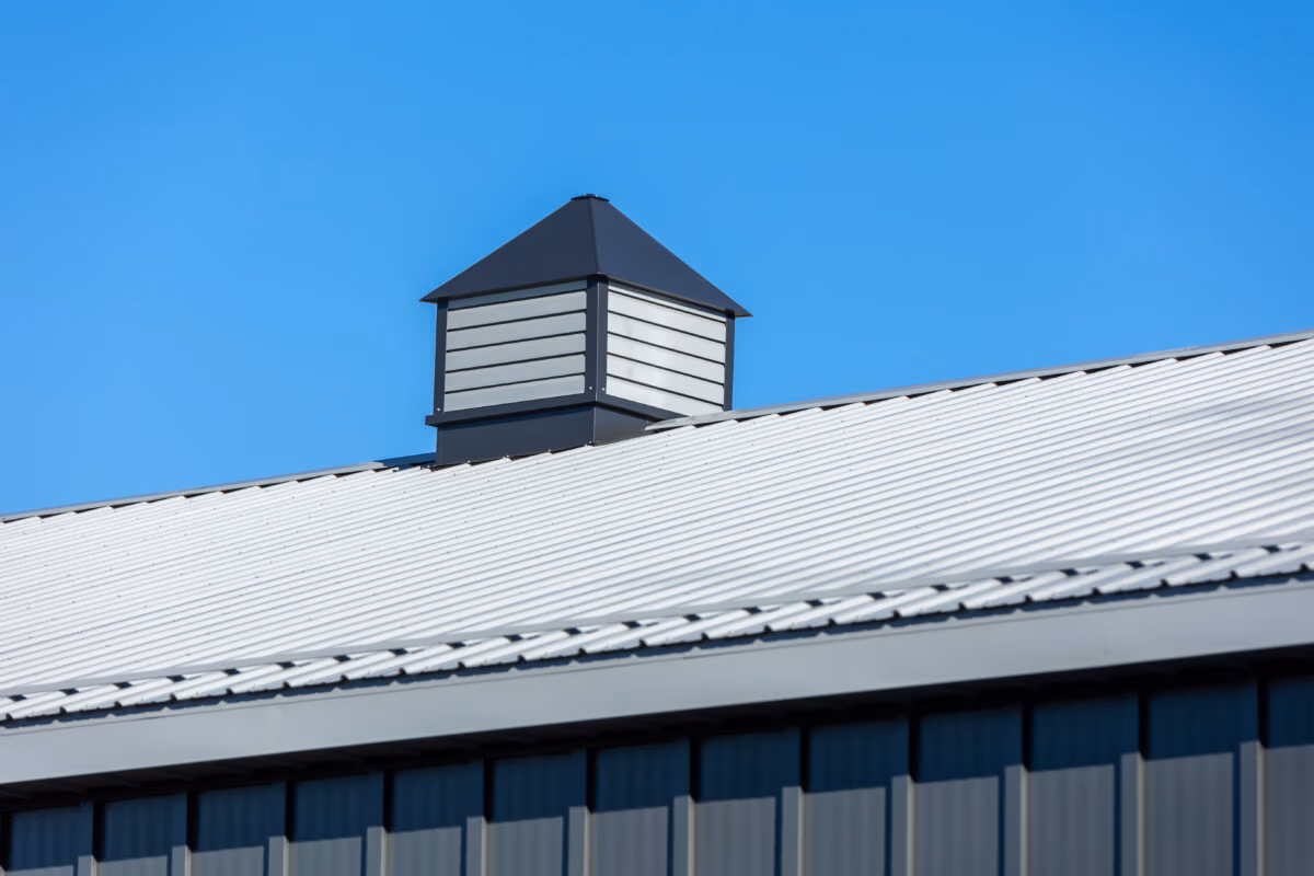 Black cupola with louvered sides mounted on a white metal roof against clear blue sky
