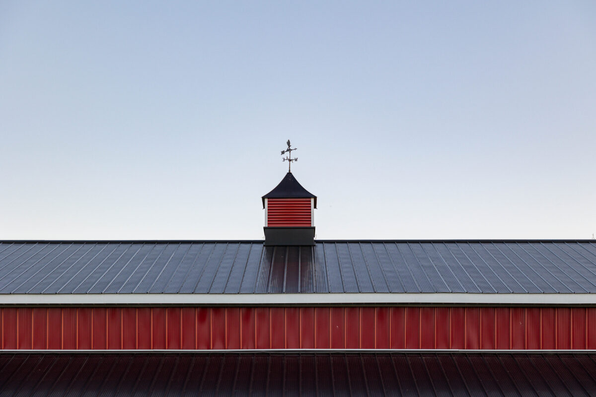 Red corrugated metal roof with black trim and a cupola topped with a weathervane spire
