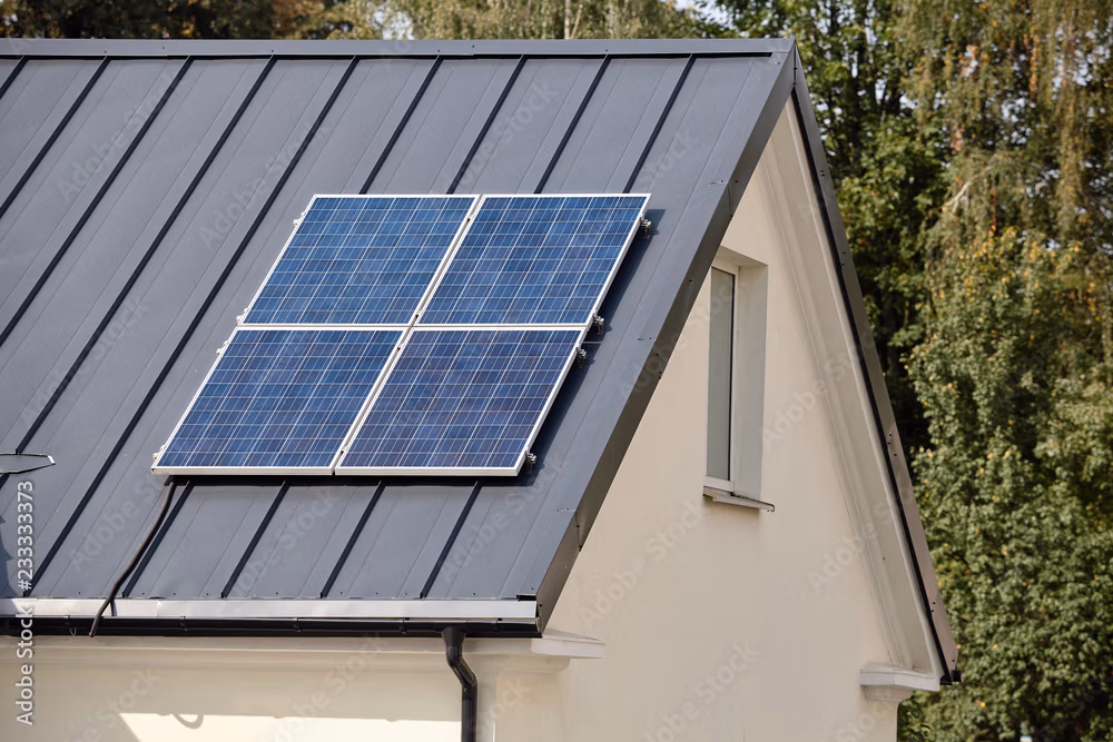 Solar panels mounted on a dark metal standing seam roof with a window and ivy-covered wall visible