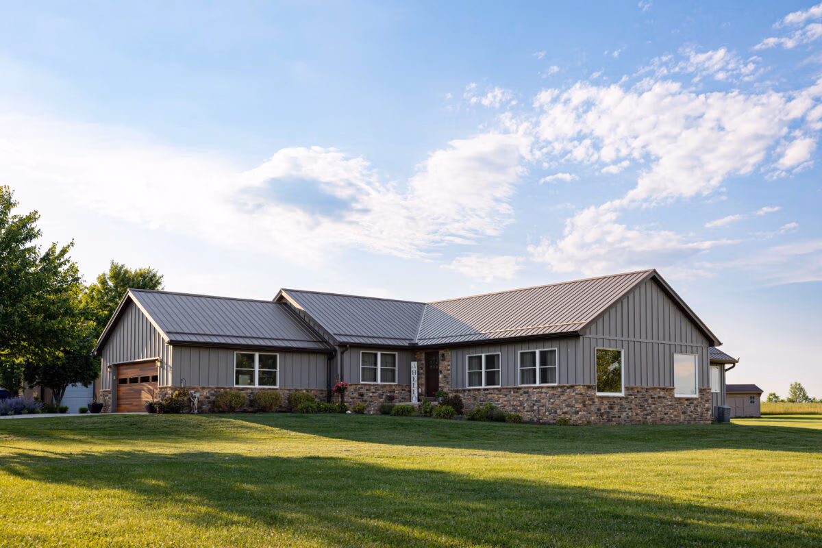 Single-story residential home with dark metal siding and metal roof on expansive green lawn