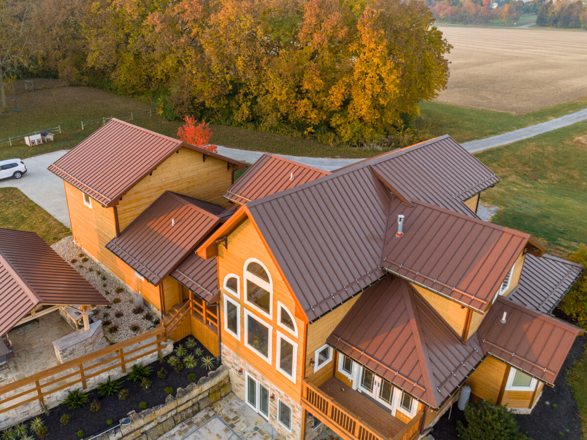 Aerial view of a two-story residential home with metal roof and coordinating metal siding, surrounded by autumn trees.